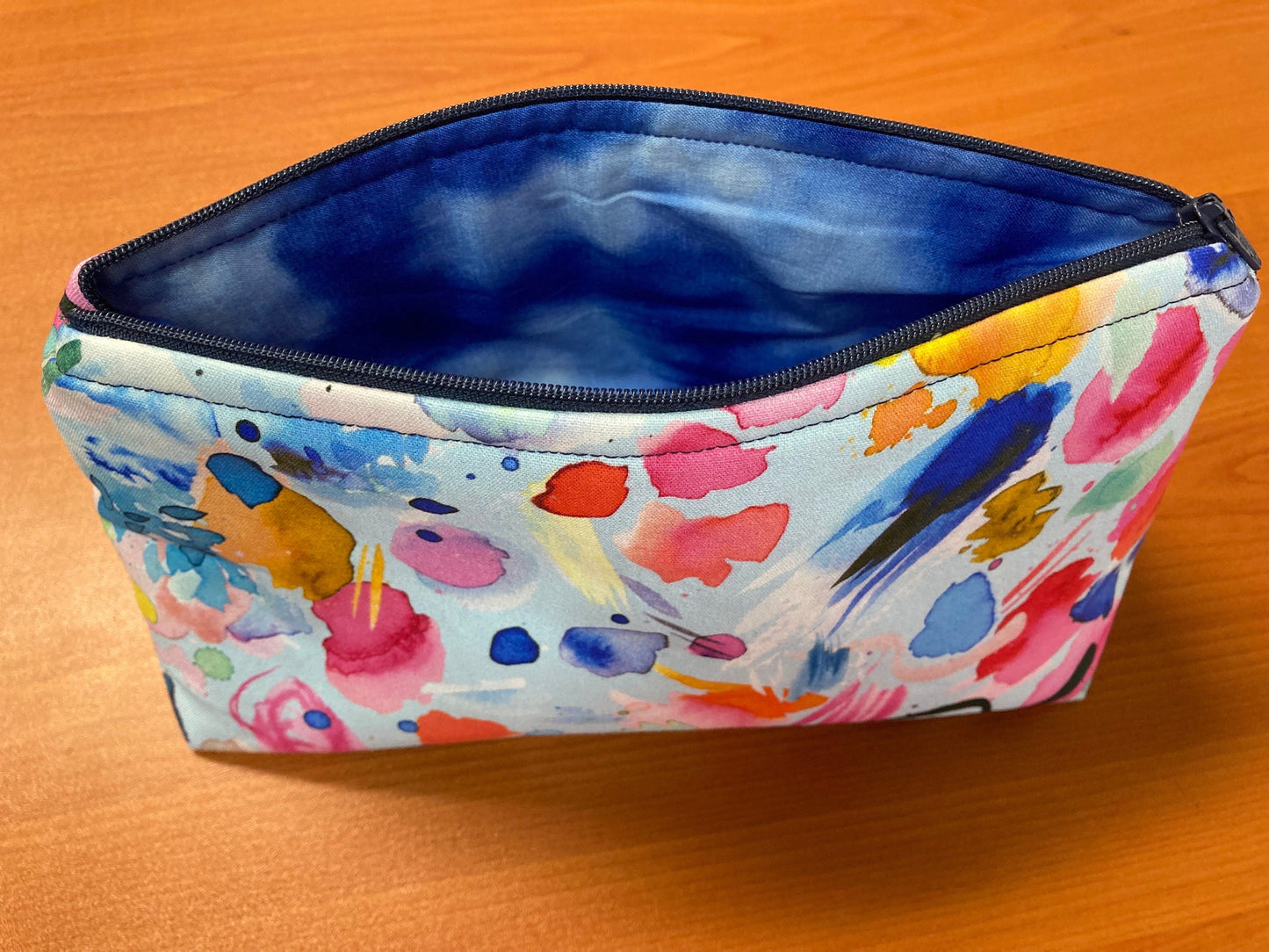 A multicoloured handmade cosmetic pouch with an open navy zipper, featuring an abstract artistic pattern.