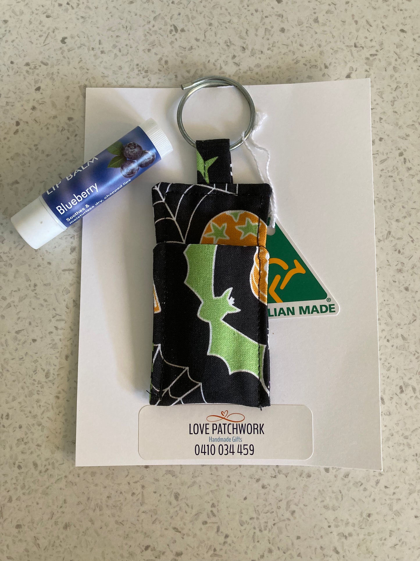 Novelty Lip Balm Keychain with green and black Halloween pattern on a card, on a light grey surface. Australian Made by Love Patchwork