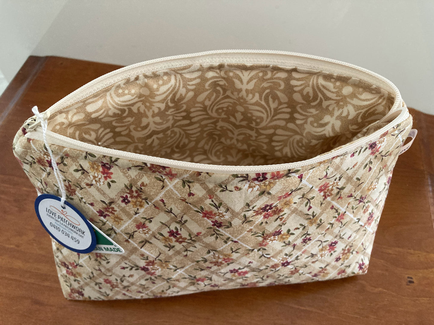 Open zippered cotton fabric floral patterned pouch with a visible Love Patchwork brand tag on a wooden surface