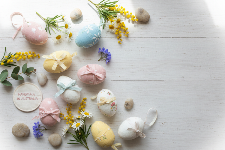 Handmade Easter gifts with pastel fabric eggs and spring flowers on wooden surface