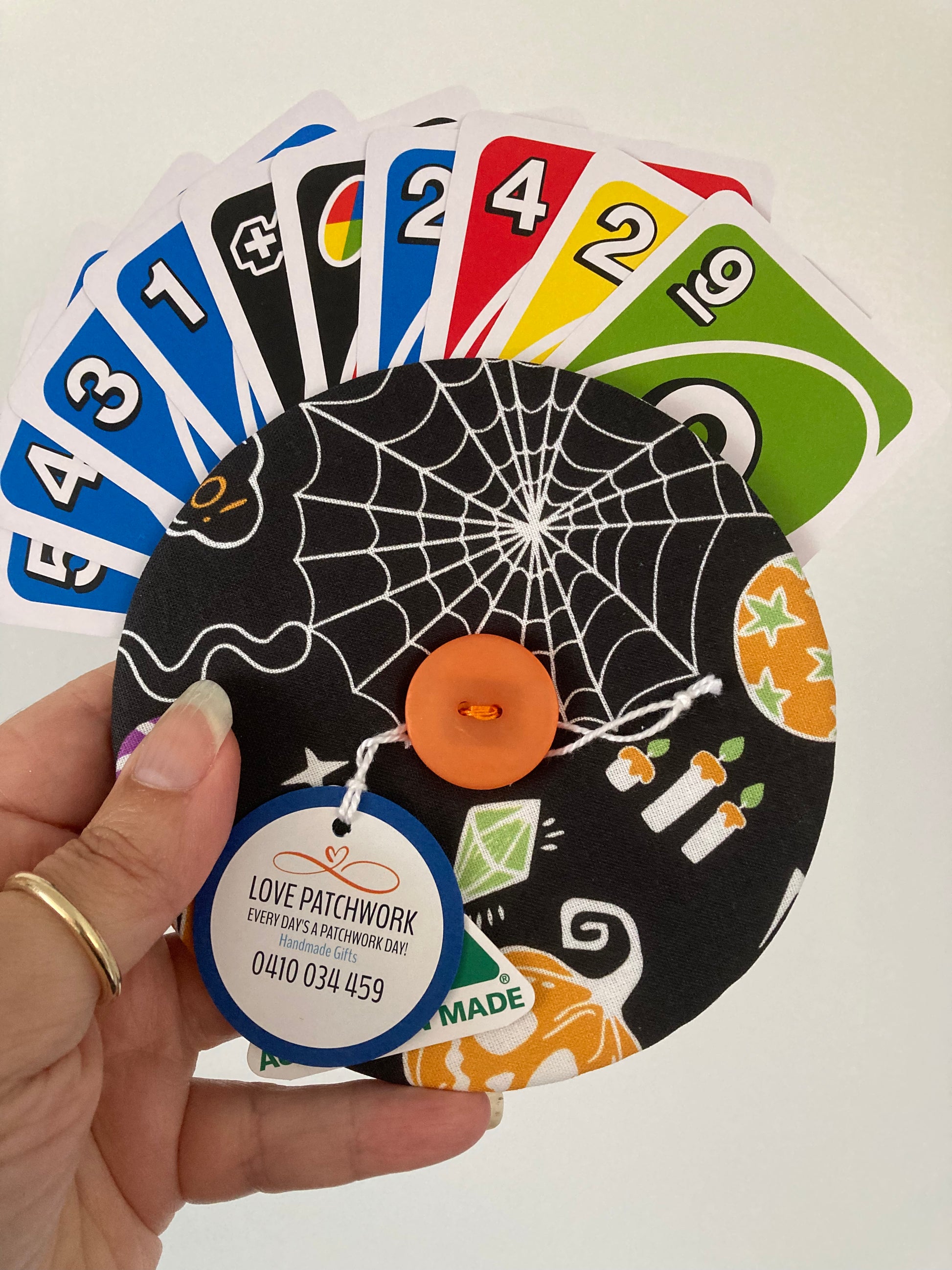 Hand holding a circular playing card holder with Halloween design assisting with holding multiple UNO cards. Australian Made by Love Patchwork