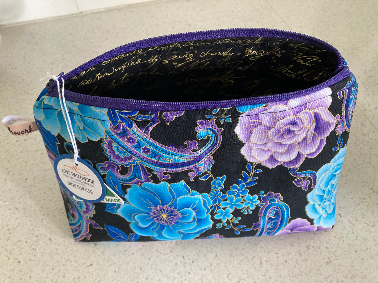 Open zippered Floral and paisley patterned pouch displaying interior black scripted interior fabric with a visible Love Patchwork brand tag on a light background