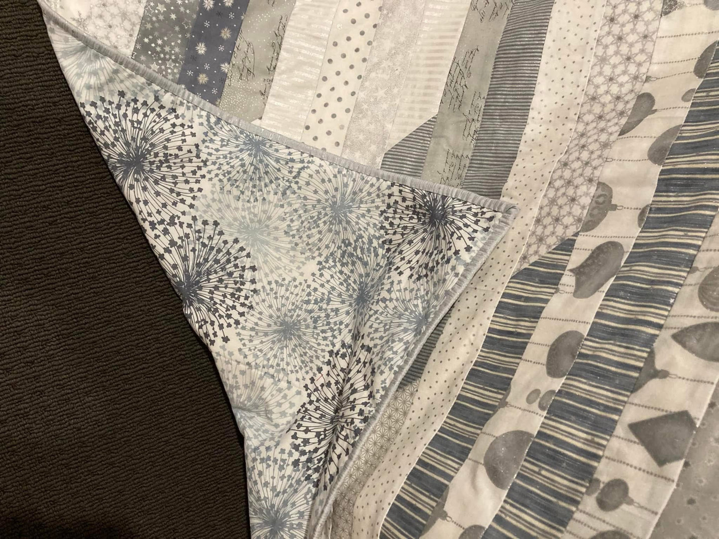 Close-up of completed baby's first Christmas quilt displaying Christmas cotton patterned fabrics, backing fabric and mitred cornered binding