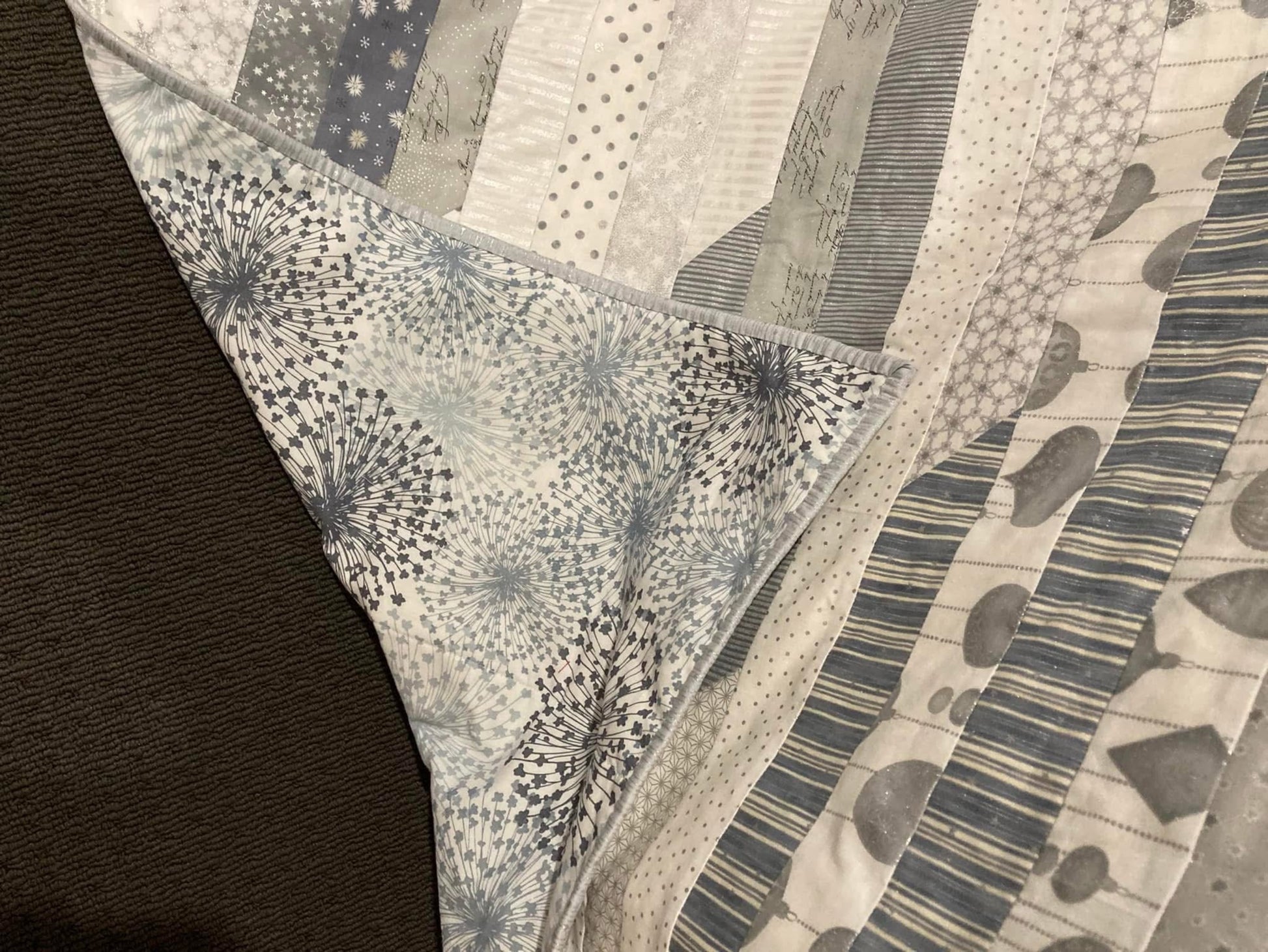 Close-up of completed baby's first Christmas quilt displaying Christmas cotton patterned fabrics, backing fabric and mitred cornered binding