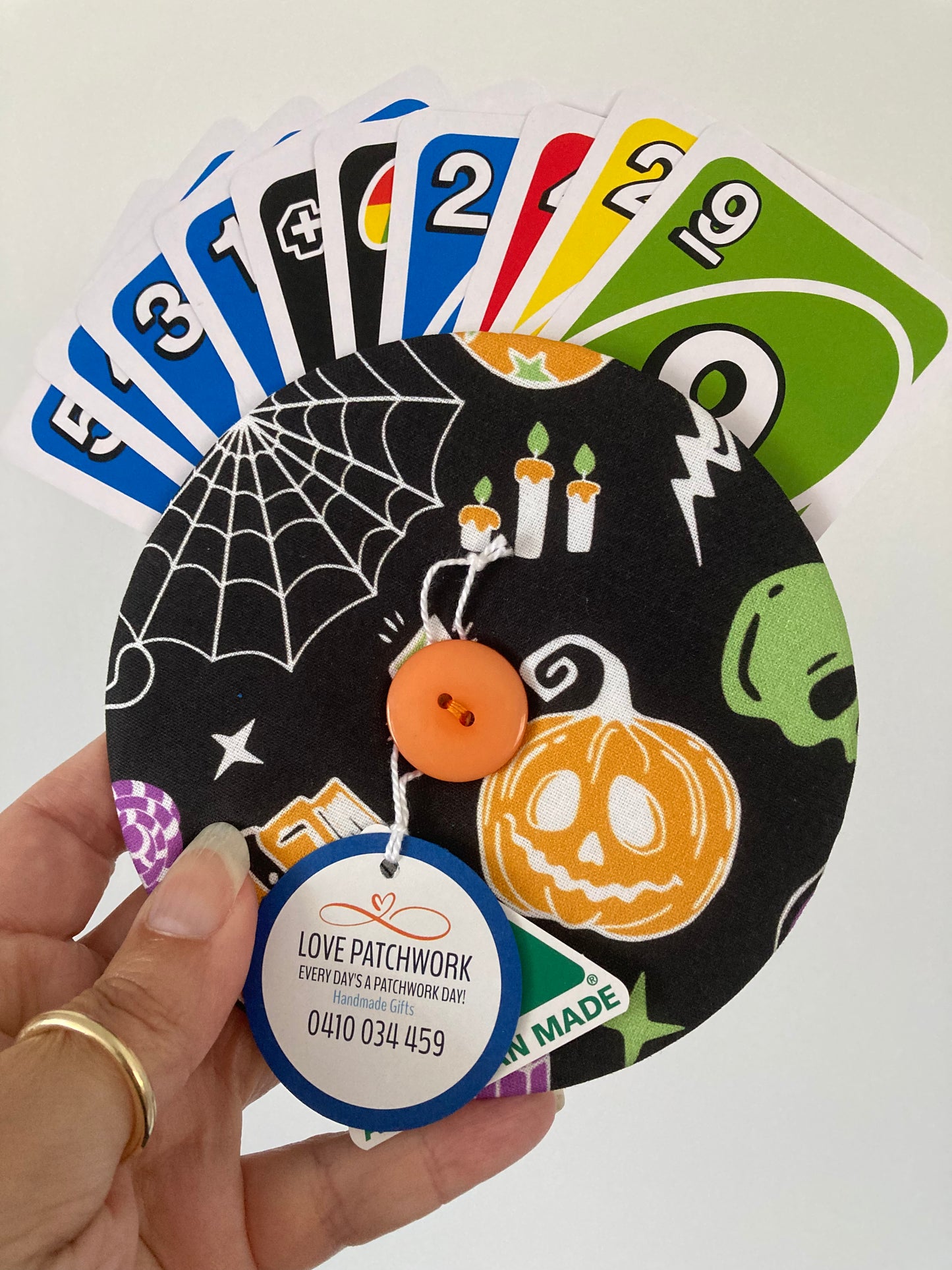 Hand holding a Halloween-themed Adaptive playing card holder with UNO cards and a round label Love Patchwork brand tag. Australian Made