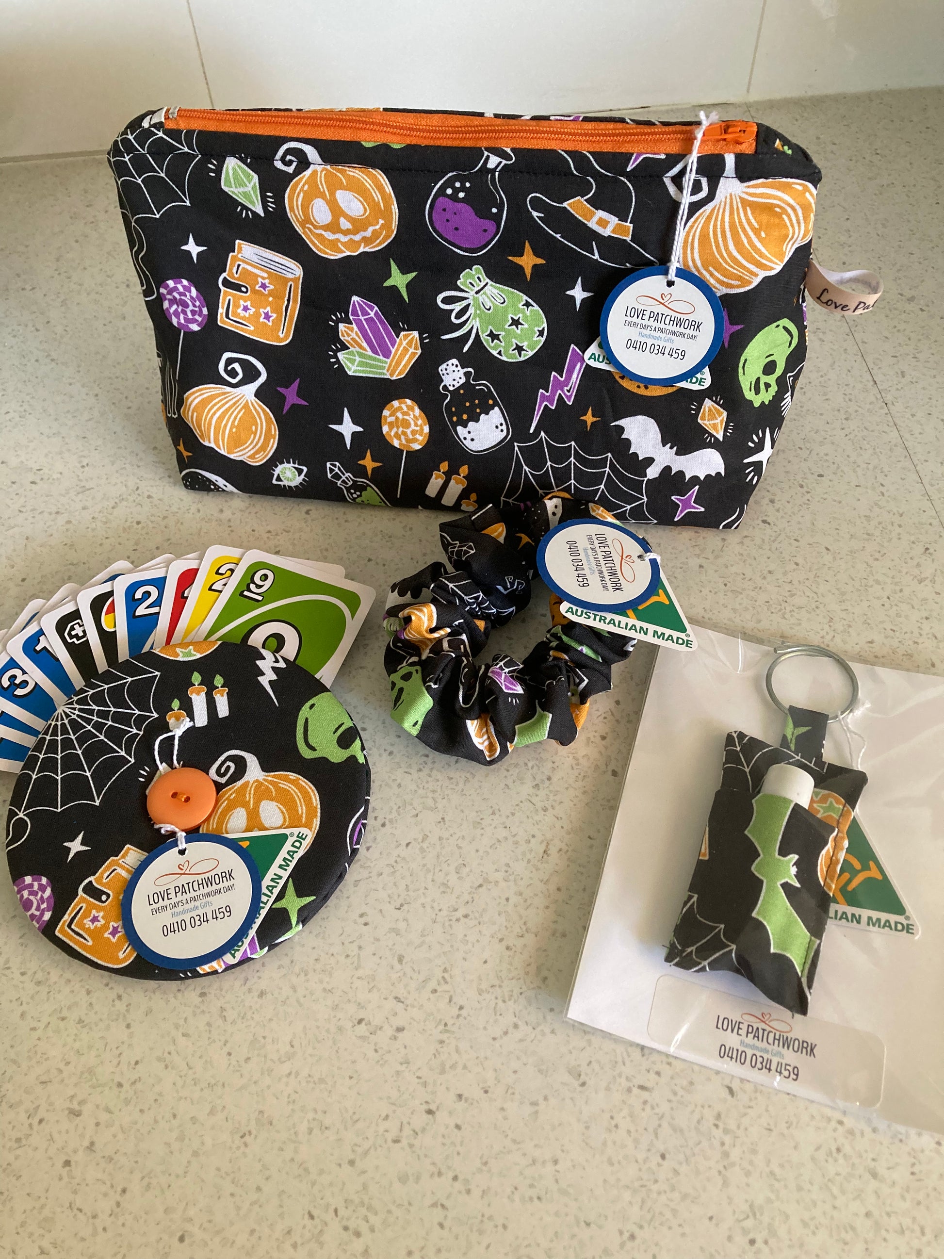 Halloween-themed gift set consisting of a pouch, hair scrunchie, playing card holder and novelty lip balm keychain on a light surface. Australian Made by Love Patchwork