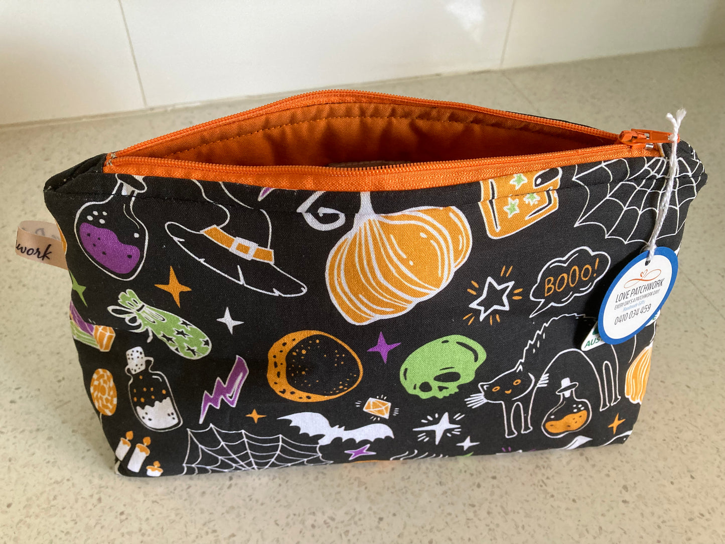 Opened Halloween-themed zippered pouch with pumpkins, ghosts, and cobwebs on a neutral background. Australian Made by Love Patchwork
